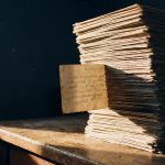 机の上に積まれた手書きのアンケート用紙の束から、1枚だけが引き出されて光を受けている